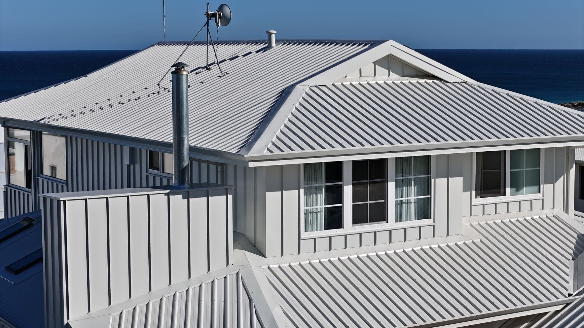 Drone view of a Surfmist metal roof and standing seam cladding on a Scarborough home, with the ocean behind, Perth